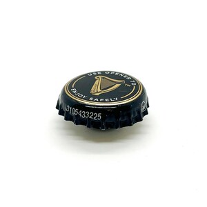 May include: A black bottle cap with gold lettering and a gold border. The cap features a harp symbol and the words "USE OPENER TO ENJOY SAFELY". The serial number "3105433225" is printed on the cap.