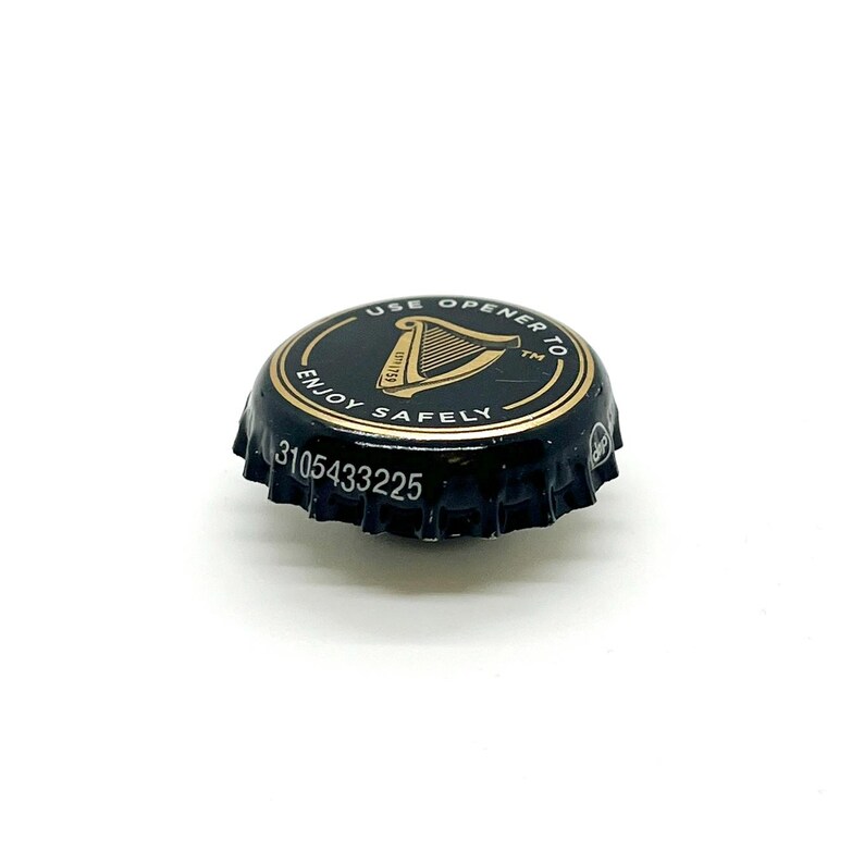 May include: A black bottle cap with gold lettering and a gold border. The cap features a harp symbol and the words "USE OPENER TO ENJOY SAFELY". The serial number "3105433225" is printed on the cap.
