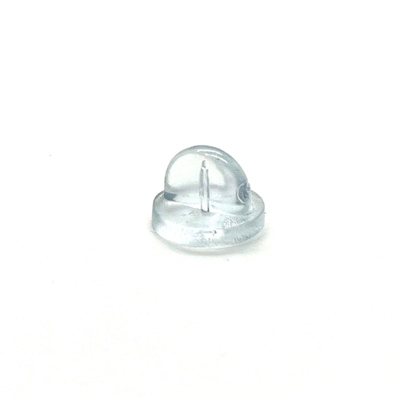 May include: A clear, transparent earring back, designed to secure earrings. The earring back is made of a soft, flexible material and has a rounded top with a post hole. The base is flat and circular.
