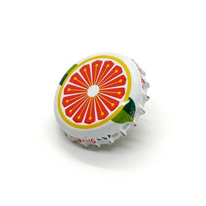 May include: A white bottle cap with a red grapefruit slice design, outlined in yellow, and green leaves. The cap has a silver, crimped edge and the word "INVIG" is visible.
