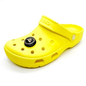May include: Vibrant yellow Crocs clog with a black and silver bottle cap charm. The charm displays the Guinness logo and the text "USE OPENER TO ENJOY SAFELY". The clog features ventilation holes and the Crocs logo.