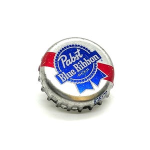 Peut inclure: Un bouchon de bouteille de bière Pabst Blue Ribbon argenté. Le bouchon présente un motif de ruban bleu avec les mots "Pabst Blue Ribbon BEER" en texte blanc. Des accents rouges sont visibles sur les bords du bouchon. Le numéro "835127" est imprimé sur le bouchon.