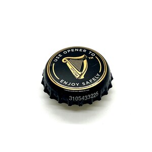 May include: A black bottle cap with gold lettering and a gold harp design. The text on the cap reads "USE OPENER TO ENJOY SAFELY" and "EST 1759". The cap also has the number "3105433225" printed on it.