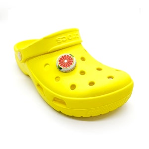 May include: A yellow clog with a grapefruit design bottle cap charm. The charm is attached to the top of the clog.