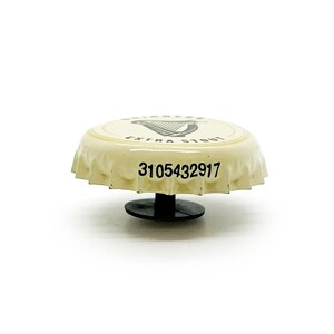 May include: A white bottle cap with a black harp logo and the text "Guinness Extra Stout". The bottle cap has a black plastic ring on the bottom and the number "3105432917" printed on the top.