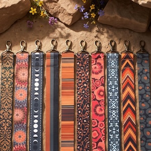May include: Ten long, flat bag straps arranged side-by-side, each featuring a unique pattern including floral, geometric, moon phase, leopard print, and striped designs. Each strap is finished with a metallic swivel lobster clasp at the top.