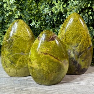 May include: Three green and brown polished gemstone eggs. The eggs are smooth and have a marbled pattern.