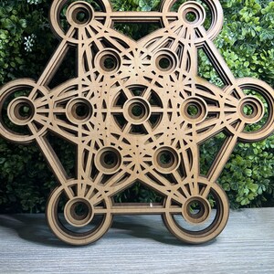 May include: A wooden geometric mandala with a complex design featuring multiple concentric circles and overlapping shapes. The mandala is made of light brown wood and has a natural finish.