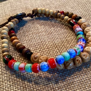 May include: A double-strand bracelet with brown wooden beads and colorful glass beads. The bracelet has a brown leather cord with a metal clasp.
