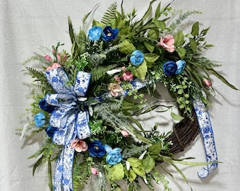 May include: A blue and white floral wreath with a blue and white ribbon bow. The wreath is made of greenery and flowers, including blue and pink roses.