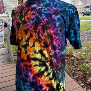 May include: A short-sleeved tie-dye t-shirt in a vibrant array of colors, including black, blue, orange, yellow, and pink. The shirt is displayed on a mannequin, showcasing its unique, swirling pattern. The t-shirt is a classic crew neck style.