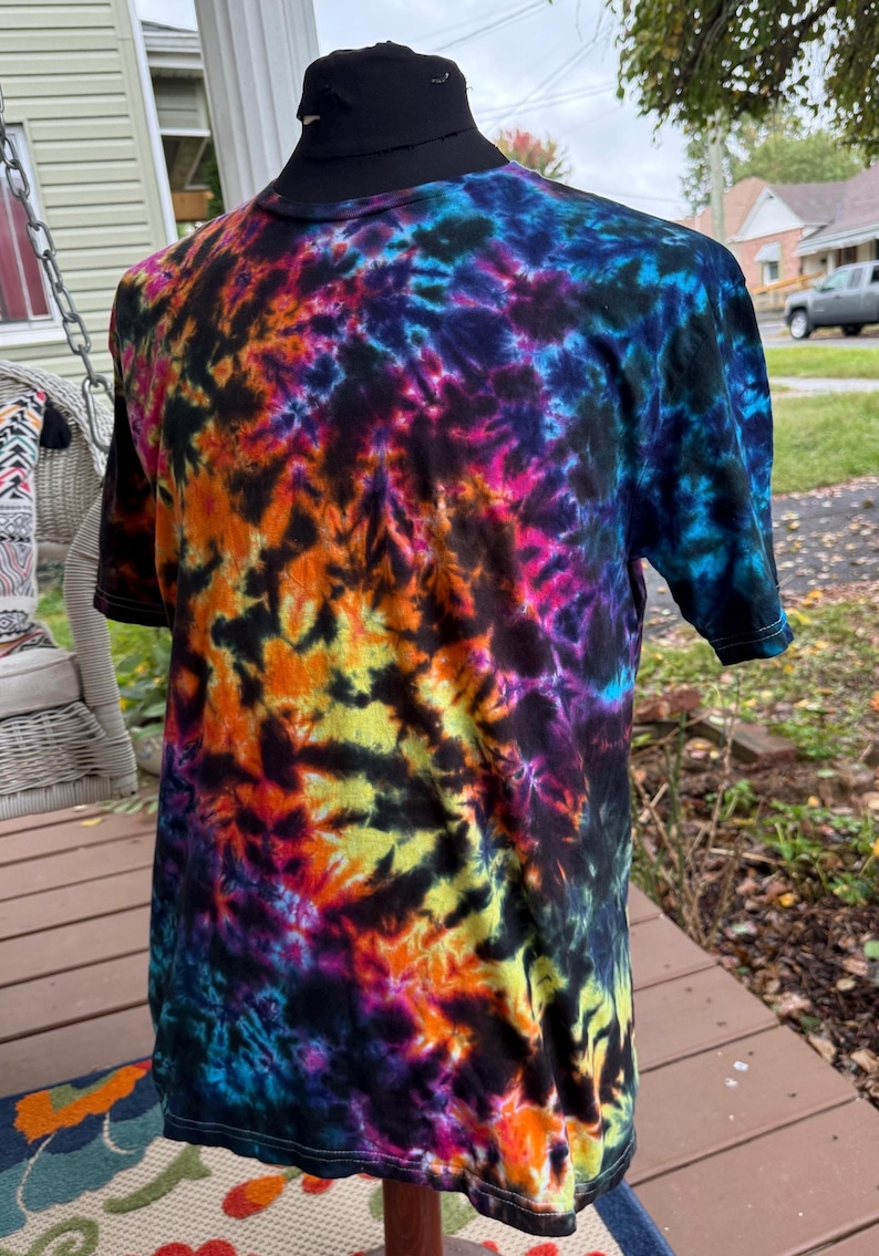 May include: A short-sleeved tie-dye t-shirt in a vibrant array of colors, including black, blue, orange, yellow, and pink. The shirt is displayed on a mannequin, showcasing its unique, swirling pattern. The t-shirt is a classic crew neck style.
