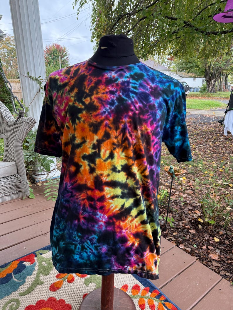 May include: A short-sleeved tie-dye t-shirt in a vibrant array of colors, including orange, yellow, pink, blue, and purple. The shirt has a black collar and is displayed on a mannequin. The tie-dye pattern is a swirling design.