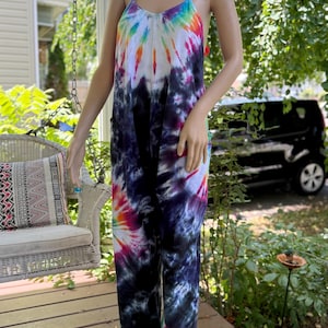 May include: A tie-dye jumpsuit in a vibrant rainbow of colors, including blue, purple, pink, orange, and white. The jumpsuit features a V-neck and spaghetti straps. The fabric is soft and flowing, perfect for warm weather.