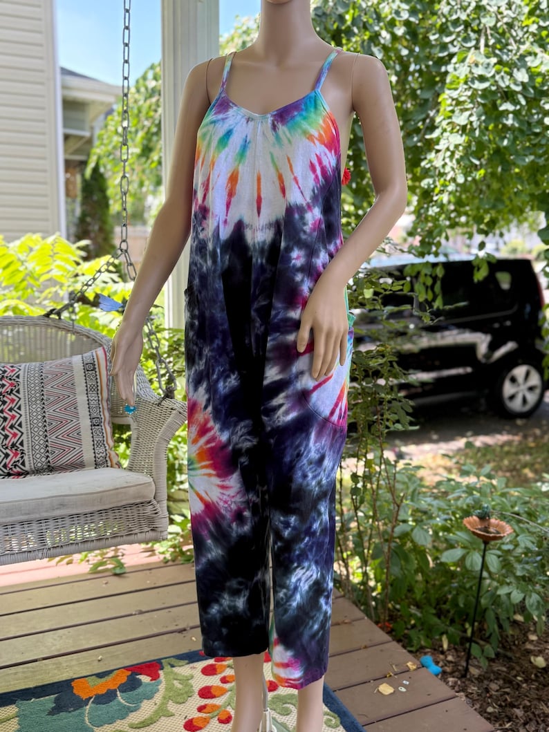 May include: A tie-dye jumpsuit in a vibrant rainbow of colors, including blue, purple, pink, orange, and white. The jumpsuit features a V-neck and spaghetti straps. The fabric is soft and flowing, perfect for warm weather.