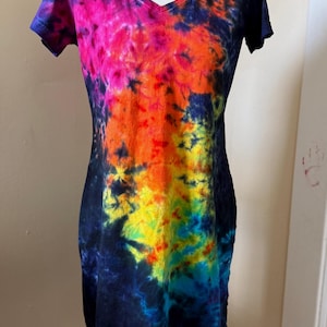 Puede incluir: Vestido con cuello en V teñido con tinte anudado en una vibrante gama de colores, incluyendo morado, rosa, naranja, amarillo y azul. El vestido tiene mangas cortas y una silueta ajustada.