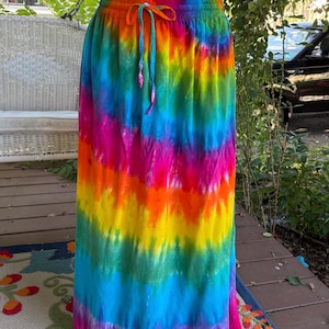 May include: A long, flowing tie-dye skirt in a vibrant rainbow of colours, including pink, orange, yellow, green, and blue. The skirt has an elasticated waistband with a drawstring. This colourful skirt is perfect for a casual, bohemian look.