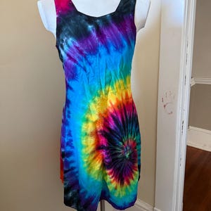 May include: A sleeveless tie-dye dress in a spiral pattern, with a vibrant mix of colours including blue, purple, yellow, and red. The dress is displayed on a white mannequin.