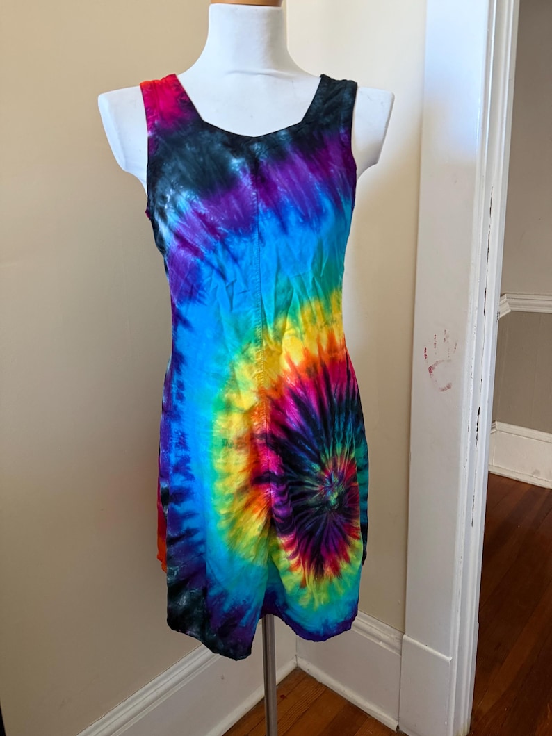 May include: A sleeveless tie-dye dress in a spiral pattern, with a vibrant mix of colours including blue, purple, yellow, and red. The dress is displayed on a white mannequin.