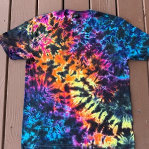 May include: A short-sleeved t-shirt with a vibrant tie-dye pattern. The shirt features a blend of colors, including black, blue, purple, pink, orange, and yellow. The tie-dye design is spread across the entire shirt, creating a psychedelic effect. The shirt is made of a soft material.