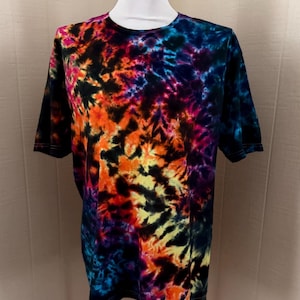 May include: A short-sleeved t-shirt with a vibrant tie-dye pattern. The shirt features a blend of colors, including orange, yellow, blue, purple, and black. The tie-dye design is displayed on a white mannequin.