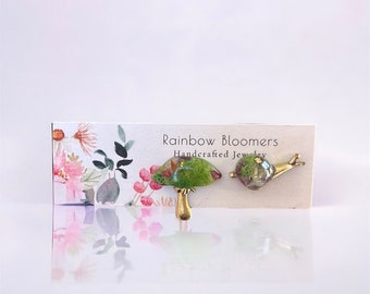 May include: A pair of handmade resin jewelry pieces, a green mushroom and a snail, on a white card with the text "Rainbow Bloomers Handcrafted Jewelry".