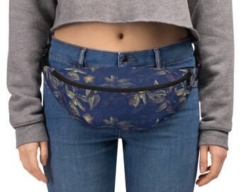 May include: A blue fanny pack with a floral pattern featuring yellow, green, and red accents. The fanny pack is worn around the waist of a person wearing a grey cropped sweater and blue jeans.