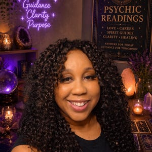 May include: A woman with curly dark hair smiles in front of a neon sign that reads "Intuition, Guidance, Clarity, Purpose." A sign behind her says "Psychic Readings" with text about love, career, and healing. Tarot cards and crystals are visible.