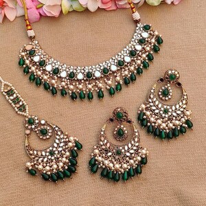 Puede incluir: Un conjunto de joyas de novia indias tradicionales que incluye un collar, pendientes y un maang tikka dorados. El conjunto est&aacute; adornado con piedras verdes y blancas, perlas y trabajo de espejo.