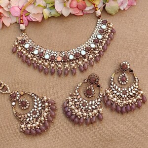 Puede incluir: Un conjunto de collar de novia indio malva y dorado con trabajo de espejo y acentos de perlas. El conjunto incluye un collar gargantilla y un par de pendientes.