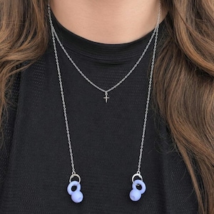 Può includere: Una collana a catena multistrato color argento con un piccolo ciondolo a croce sulla catena più corta e due ciondoli circolari in silicone color viola chiaro alle estremità della catena più lunga, progettata per tenere al sicuro gli auricolari.