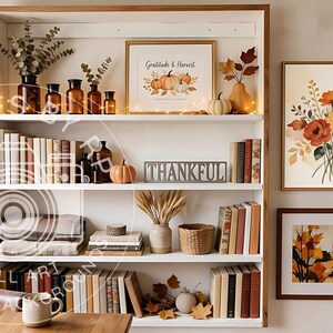 May include: A white wooden bookshelf filled with books, glass bottles, small pumpkins, and a sign reading THANKFUL. Above the shelf, a framed print says Gratitude & Harvest. Two additional framed art prints hang on the wall featuring floral and autumn themes.