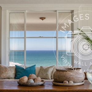 Puede incluir: Un salón con una mesa de centro de madera, un sofá con cojines decorativos y una gran ventana con vistas al mar. También hay una obra de arte enmarcada y objetos decorativos. Un jarrón con vegetación está sobre la mesa.