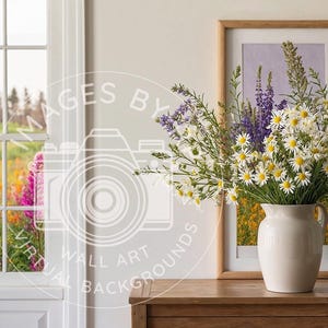 May include: A white ceramic pitcher filled with a bouquet of white daisies and purple wildflowers. The flowers are arranged in a vase on a wooden table in front of a window with a view of a field of wildflowers.
