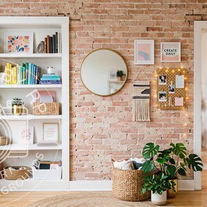 May include: A white bookshelf filled with colorful books and plants stands against a red brick wall. A round gold mirror, a pegboard with photos and the text CREATE DAILY, and a woven wall hanging are mounted on the wall near a potted plant.