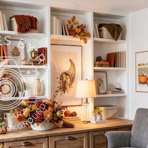 May include: A white built-in bookshelf filled with books, autumn-themed decor, and artificial fall foliage. The shelves feature pumpkins, vases, and framed art prints. A wooden desk sits below with a lamp and a grey upholstered armchair nearby.