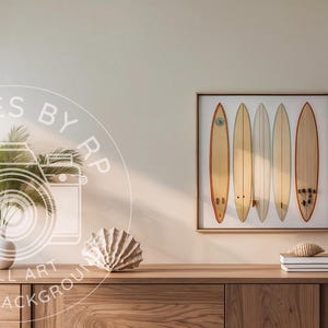 May include: A framed wall art print featuring six surfboards in various shades of tan and brown. The artwork hangs above a wooden cabinet, next to a white lamp and decorative items. The overall theme is coastal decor.