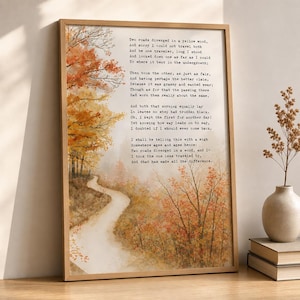 May include: A framed wall art print featuring a winding path through an autumn forest with orange and yellow trees. The text of Robert Frost's poem, The Road Not Taken, is printed in black typewriter-style font over the watercolour landscape scene.
