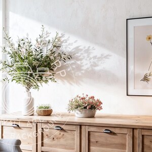 Puede incluir: Escena interior luminosa con un mueble de madera con cajones, adornado con objetos decorativos. Una impresión botánica enmarcada, una lámpara y plantas en macetas están encima. Un jarrón con vegetación y un pequeño arreglo floral completan la decoración.
