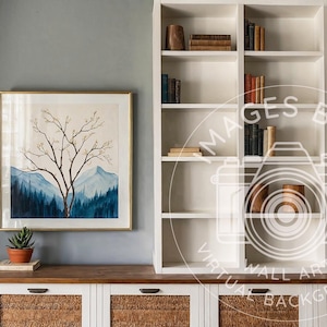 May include: A room interior with a wooden cabinet, a framed watercolour painting of a tree and mountains, a wooden lamp, and a white bookshelf filled with books and decorative items. The room has a neutral colour palette.