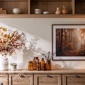 May include: A wooden console table features a white vase with autumn foliage, several amber glass bottles, and a framed forest landscape print. Above, a wooden shelf holds books, bowls, gourds, and a basket. A lamp sits on the right side of the table.