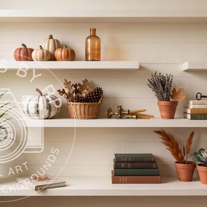 May include: Three white shelves holding decorative items including small pumpkins, a glass bottle, a woven basket with pinecones, a metal watering can, stacks of books, terracotta pots with plants, and a brass candle holder against a wall.