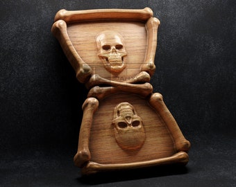 Könnte beinhalten: Eine Sanduhr aus Holz mit zwei geschnitzten Schädeln und gekreuzten Knochen. Die Sanduhr ist aus hellbraunem Holz gefertigt und hat eine natürliche Oberfläche.