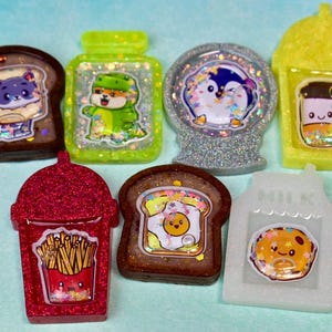 May include: Eight resin charms with glitter and various cartoon characters. The charms are shaped like a cup of coffee, a glass of milk, a cup of fries, a glass of milk, a snow globe, a bottle of juice, a slice of toast with an egg, and a slice of toast with a cat.