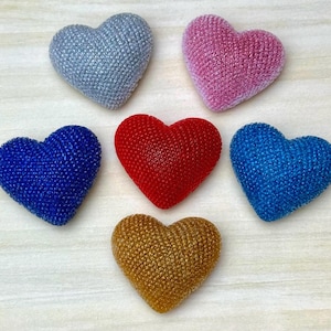 May include: Six heart-shaped objects with a textured, glittery surface. The collection includes one silver, one pink, one red, one gold, one royal blue, and one light blue heart, all arranged in a cluster on a light-colored surface.