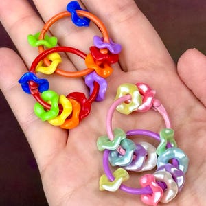 May include: Two circular metal rings featuring multiple small, wavy-edged flower-shaped beads in various colors. One ring set displays vibrant primary colors like red, orange, yellow, green, blue, and purple, while the other features pastel tones.
