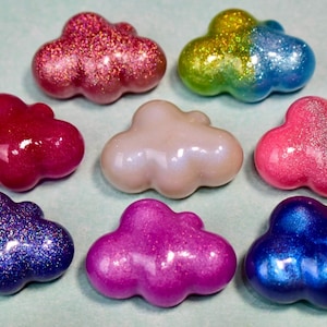 May include: Eight cloud-shaped ornaments with smooth, rounded surfaces. The collection includes pieces in glittery red, a yellow-to-blue gradient, deep magenta, pearlescent white, bright pink, dark purple glitter, vibrant fuchsia, and metallic blue.