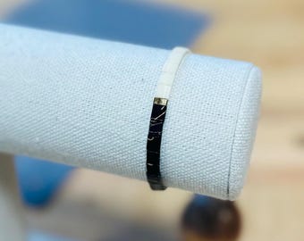 May include: A black and white bracelet with a gold accent. The bracelet is made of small, square tiles.