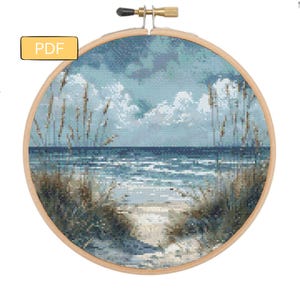 Può includere: Uno schema di punto croce che rappresenta una scena di spiaggia con erbe alte in primo piano, un oceano blu e un cielo nuvoloso.