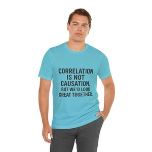 May include: A light blue t-shirt with the text "CORRELATION IS NOT CAUSATION, BUT WE'D LOOK GREAT TOGETHER" in black. The shirt is being worn by a person.